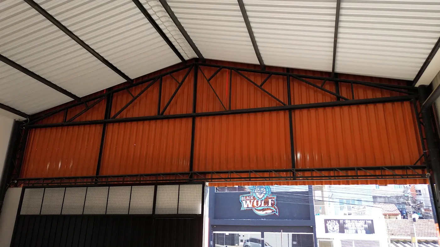 Telhado metálico de duas águas em telha trapezoidal branca, com tesoura aparente, sobre uma loja